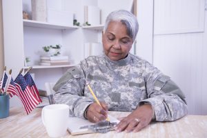 Female recruiter reviews applications. Senior soldier reviews paperwork sits at desk. Cup of American Flags on her desk.